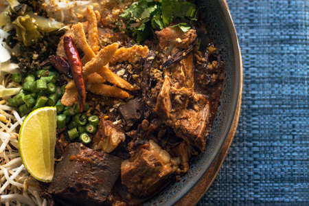Khanom Jeen Nam ngiao (Spicy Rice Noodle Soup) with spicy pork sauce on dark blue table cloth, Traditional northern Thai cuisine. overhead viewの写真素材