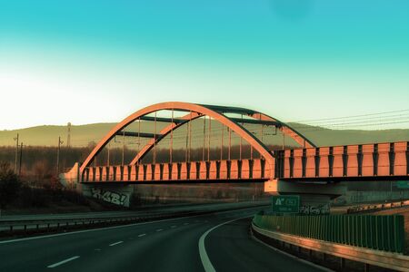 Copper-colored Railroad bridge over a Highway on a vibrant sundown colored Skyの写真素材