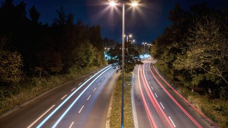 A long exposure shot of a four-lane road at night with glowing vehicle lights