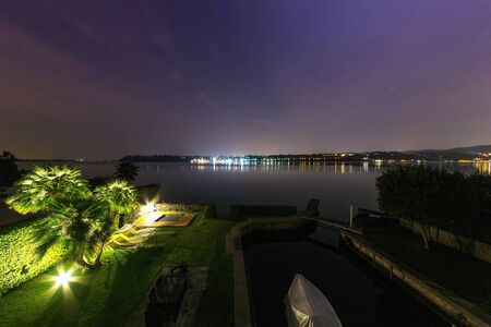 A view of Lake Garda with the illuminated lights of the city on the other bank at nightの写真素材