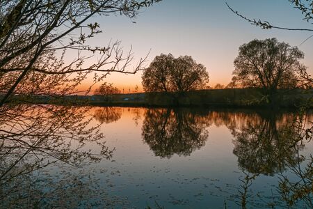 A beautiful orange sunset in the silhouette of trees and bushes on a small lakeの写真素材