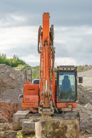 A red excavator on a pile of gravel and earthの写真素材