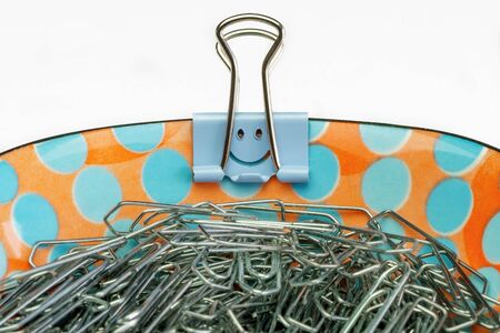 A porcelain bowl with paper clips and a blue smiley paper clip on the edge, white backgroundの写真素材