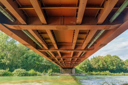 Below a rusty metal railroad bridge under which a river runsの写真素材