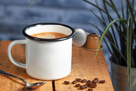 A white coffee cup with cream coffee stands on a colored wooden wooden surface. Coffee beans are next to itの写真素材