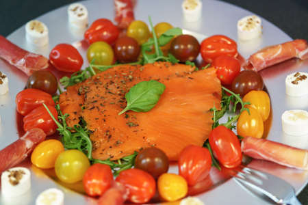 A cold meat platter with fresh salmon, tomatoes and rocket salad arranged on a silver plateの写真素材