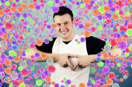 Young man making heart sign with palms with colored balls in the backgroundの写真素材