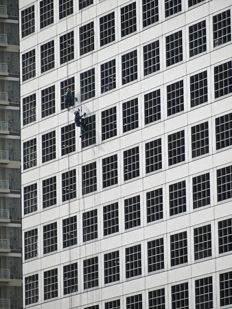two worker  climb for cleaning outside high buildingの写真素材