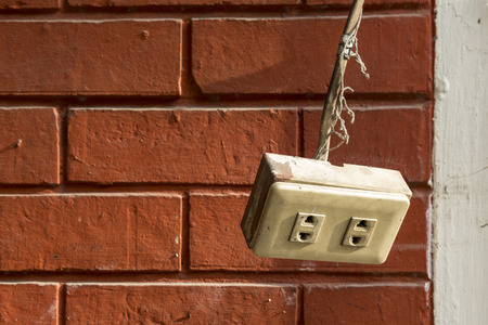 hanging of old plug socket on red brick wall in sunlightの写真素材