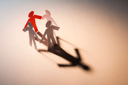 red figure in closed joining of four white paper figure in hand down posture on white background. in concept of business, cooperation and leadership.の写真素材