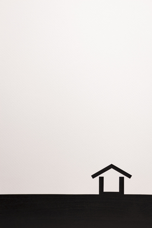 paper cutout in minimal house shape border with white background by dark brown wooden texture, for home and insurance conceptual.の写真素材