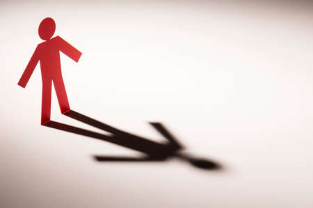 red paper cutout in hand down figure shape stand on light with shadow on white background, in...