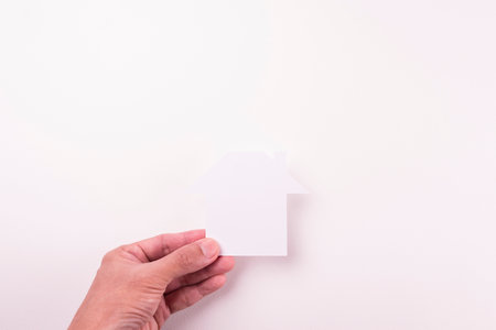 top view of  holding cutout white paper plain house by fingers on white paper background in concept of business banking and insurance.の写真素材