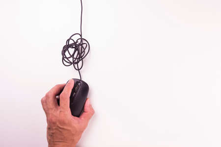top view of male left hand clicking computer mouse with tangled wires on white background with copyspace, The concept of working, obstacle and problem.の写真素材