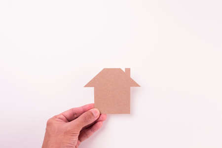top view of holding cutout brown paper plain house by fingers on white paper background in concept of business, banking and environment.の写真素材