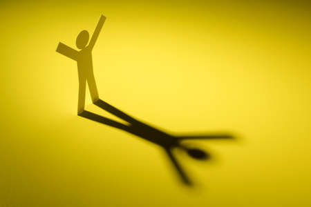 white paper cutout in hand up figure shape stand on yellow light with shadow on white background, in...