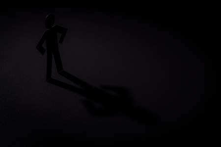 black paper cutout in akimbo figure shape stand on light with shadow on black background, in concept of loneliness, badness and  strength.の写真素材