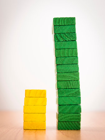 high - low two step bar graph of stack color wooden toy blocks on white background, compair between yellow and green colorの写真素材