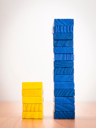 high - low two step bar graph of stack color wooden toy blocks on white background, compair between yellow and blue color in concept of education and business.の写真素材
