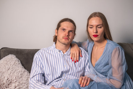 A harmonious serious couple in light blue clothes is sitting on a sofa, hugging each other. copyspace. background for quotes. high quality photoの写真素材