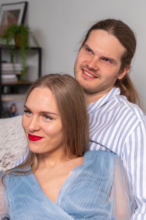 Happy couple with beautiful long hair in light blue clothes, smiling and looking ahead. A book shelf in the background. high quality photoの写真素材