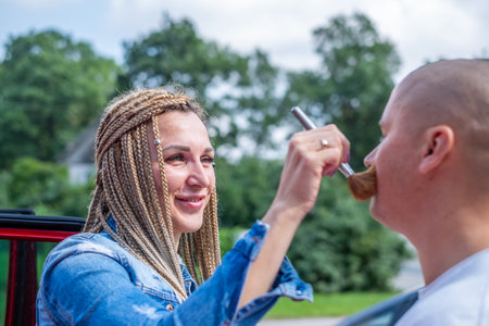 A woman with African braids applies powder to a man face with a powder brush. Copy space. High quality photoの写真素材