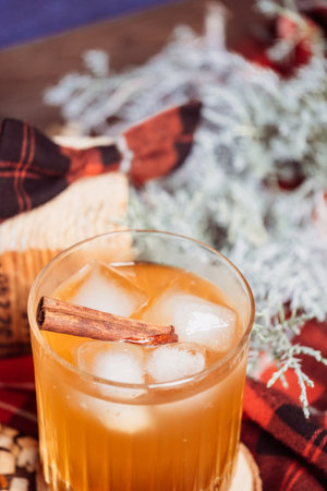 Strong whiskey in a glass with ice and a cinnamon stick with a juniper branch in the background in the Christmas mood. Red black checkered bow on a wooden pad. copyspace. high quality photoの写真素材