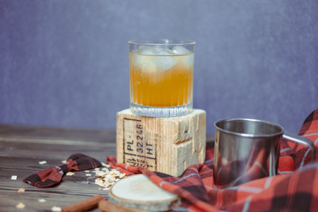 Strong whiskey in a glass with ice and a cinnamon stick with a juniper branch in the background in the Christmas mood. Red black checkered bow on a wooden pad. copyspace. high quality photoの写真素材