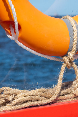 A lifebuoy is attached to a bright orange wooden frame with linen ropes, its section visible. Dark blue sea in the background. Copy space. High quality photoの写真素材