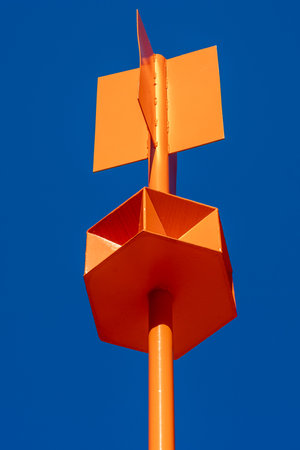 Industrial, complex shape, metal, orange sea buoy. An unpainted metal pipe in the foreground. Clear,...