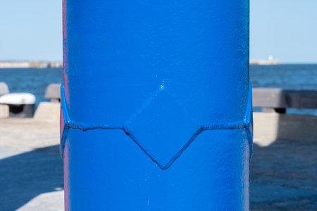 A huge metal blue pipe on the seashore. In the background, a light pavement, a wooden fence and the sea. Copy space. Background for quotes. High quality photoの写真素材