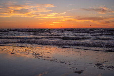 A peaceful, meditative, quiet moment - the sun is already over the horizon, white waves in the sea and orange-yellow clouds in the backgroundの写真素材