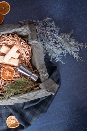 A box of Christmas gift cookies filled with shredded paper on a blue background. Alcohol jigger on a juniper branch. Copy spaceの写真素材