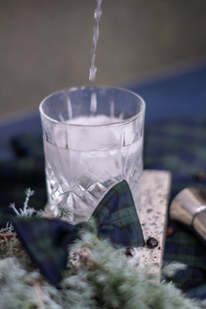 Crystal glass with gin tonic cocktail with rosemary branch and ice, checkered bow, alcohol jigger and juniper branch in the background, Christmas moodの写真素材