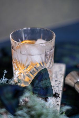 Crystal glass with gin and tonic cocktail with orange slice, rosemary branch and ice, checkered bow, alcohol measuring cup and juniper branch in the background, Christmas mood. Copy spaceの写真素材