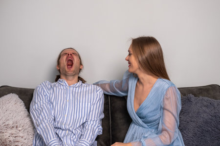 A sleepy man in a striped shirt yawns and an ironic woman with long hair, bright red nails, in a pale blue dress. Copy space. Background for quotes. High quality photoの写真素材