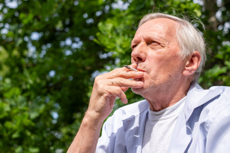 An old man with a cigarette in the park takes a puff of cigarette smoke and reflects on life,...