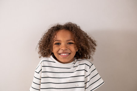 A cute and adorable smiley African American girl with curly hair and a white tshirt on a white...