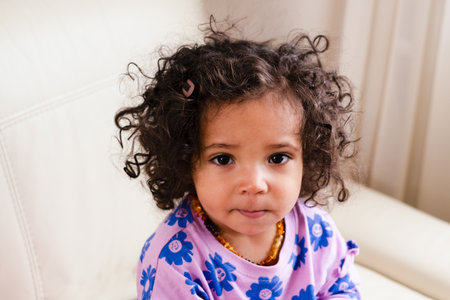 A African American thoughtful toddler with soulful eyes and curly locks sits comfortably, in a purple shirt, ideal for themes around National Siblings Day. High quality photoの写真素材