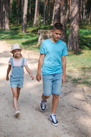 A teenage boy in a blue T-shirt walking with a young girl in denim overalls. sibling connection, ideal for National Siblings Day, or brother and sister bonds and friendships. High quality photoの写真素材