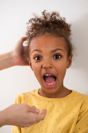 Surprised girl with wide eyes and open mouth, funny expression, hand in her curly hair, wearing a...