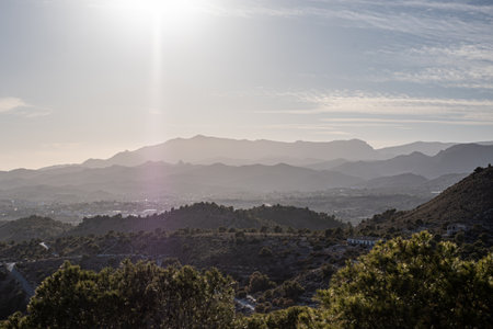 Sunrise over a layered mountain range with foreground of darkened vegetation, casting a warm glow and long shadows. High quality photoの写真素材