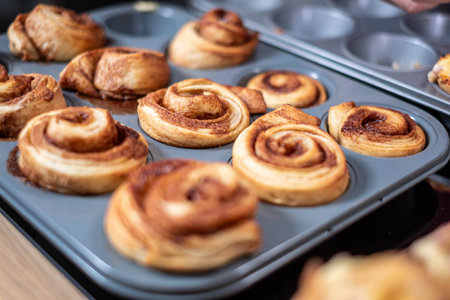 Freshly baked cinnamon rolls cooling in a muffin tin, with a golden cinnamon swirl visible, kitchen setting, delicious homemade desserts. High quality photoの写真素材