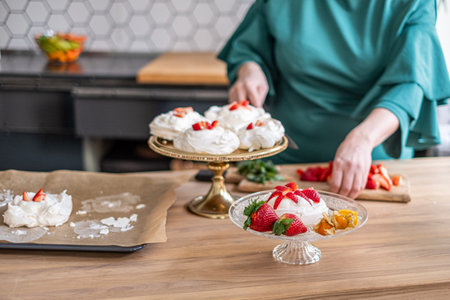 Person preparing pavlovas with fresh strawberries, kitchen setting. Ideal for a cooking tutorial. High quality photoの写真素材