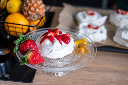 delectable pavlova adorned with strawberries rests on a glass plate, with a basket of pineapples and citrus fruits adding a vibrant backdrop. culinary guides and dessert promotions. High quality photoの写真素材