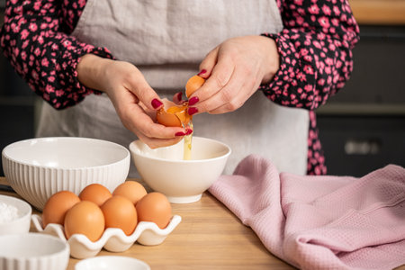 In a cozy kitchen, a cook skillfully separates an egg yolk from the white, surrounded by essential baking ingredients for a pastry recipe. High quality photoの写真素材