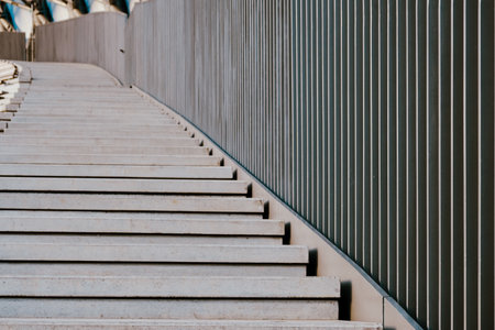 A series of smooth, gray concrete steps curves gently upward, bordered by a clean-cut metallic railing, indicating a contemporary architectural design in an urban environment.の写真素材