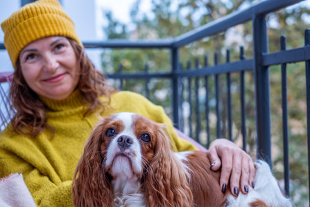 Woman in a yellow sweater relaxes on a balcony with her dog, wrapped in a blanket, embracing the autumn atmosphere and the joy of companionshipの写真素材