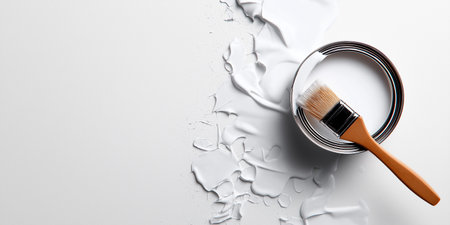 White paint flows from a can onto a flat surface. A brush lies nearby as paint drips create a mess. This shows an indoor painting activity taking place.の写真素材