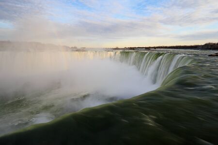 Water over Niagara Falls with a rainbow risingの写真素材